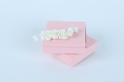 A pink gift box with a delicate white flower decoration on top, set against a plain white background.
