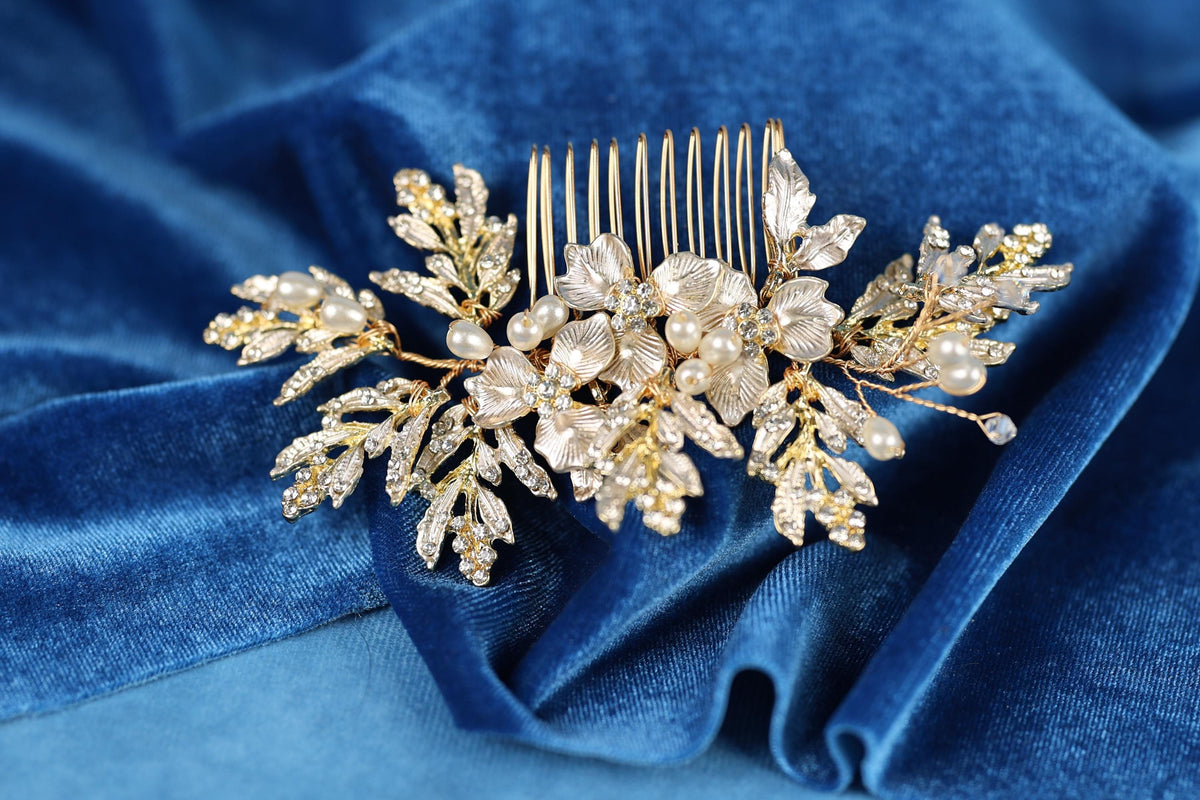 A decorative gold hair accessory with white pearls and leaves rests on a blue velvet background.
