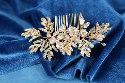 A decorative gold hair accessory with white pearls and leaves rests on a blue velvet background.