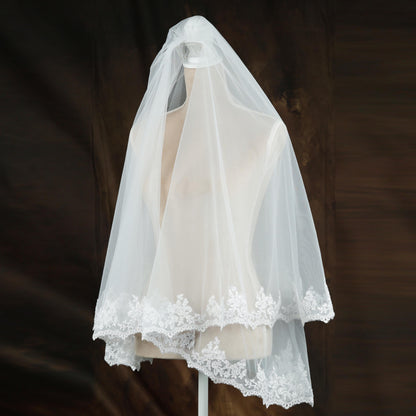 A white wedding veil with a delicate lace trim is displayed on a mannequin head against a dark background.