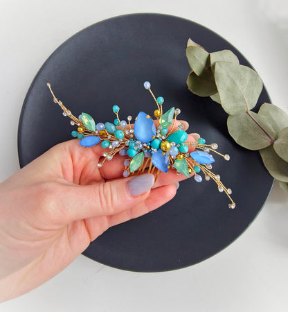 a hand holding a blue and green flower brooch