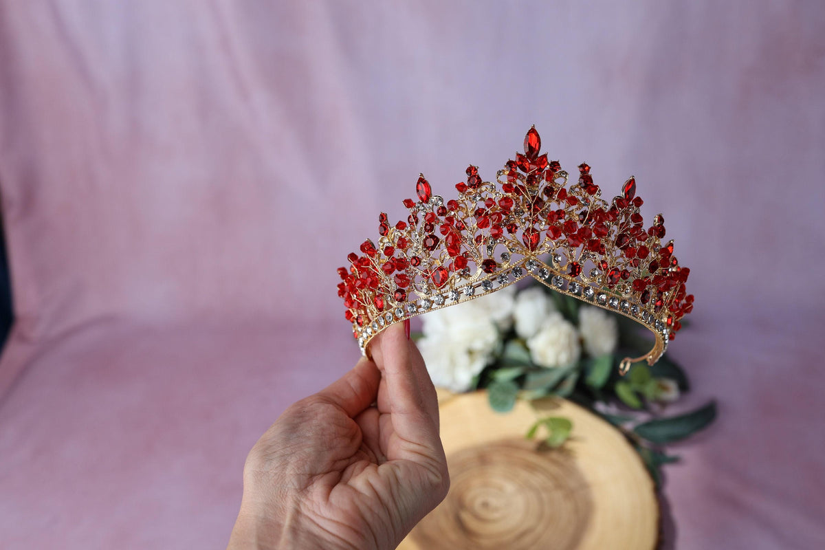 a hand holding a tiara with red stones on it