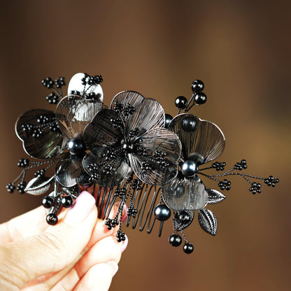 A hand holding a decorative black hair accessory with intricate floral and leaf designs.