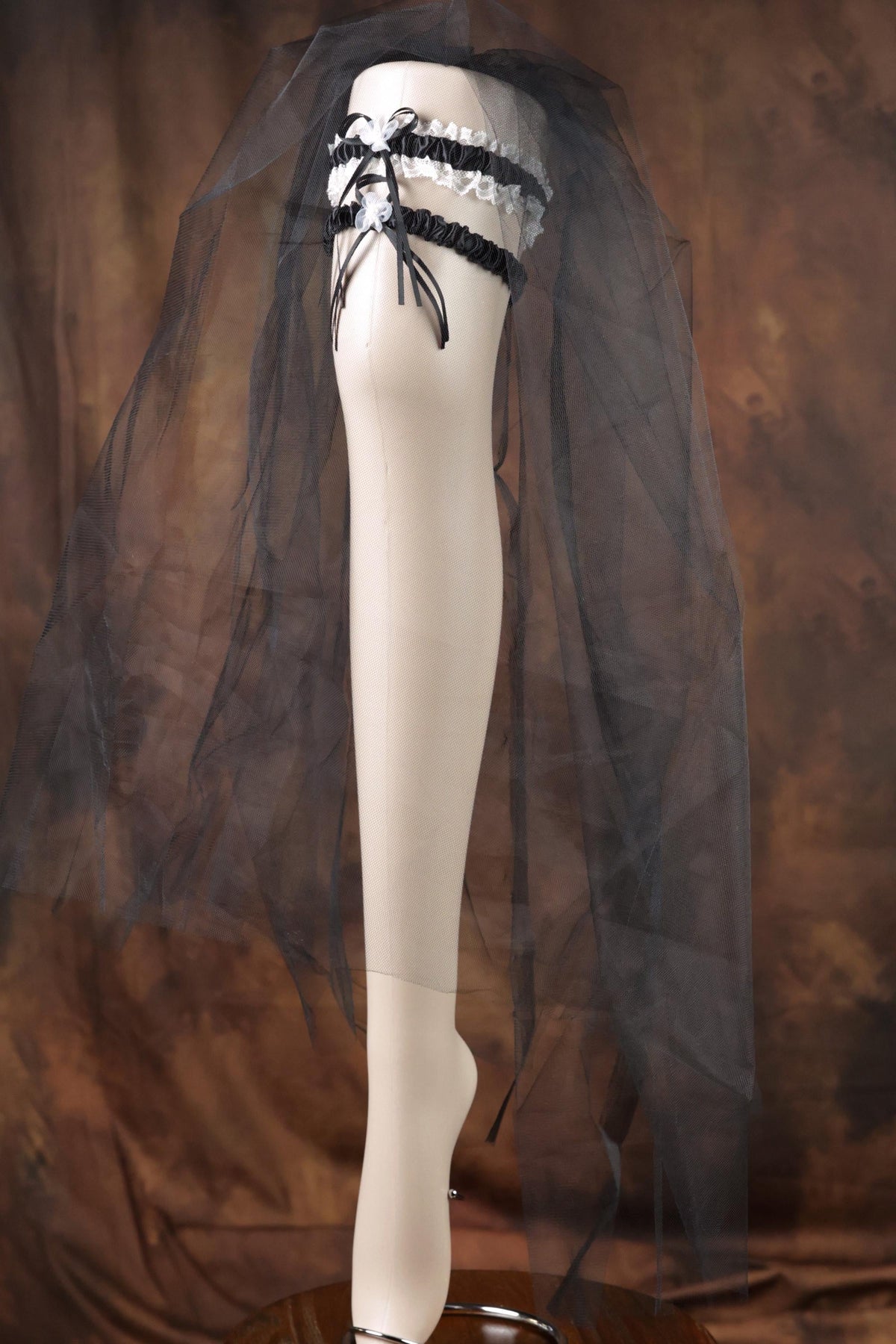 A mannequin leg wearing a black and white lace garter belt and a black veil.