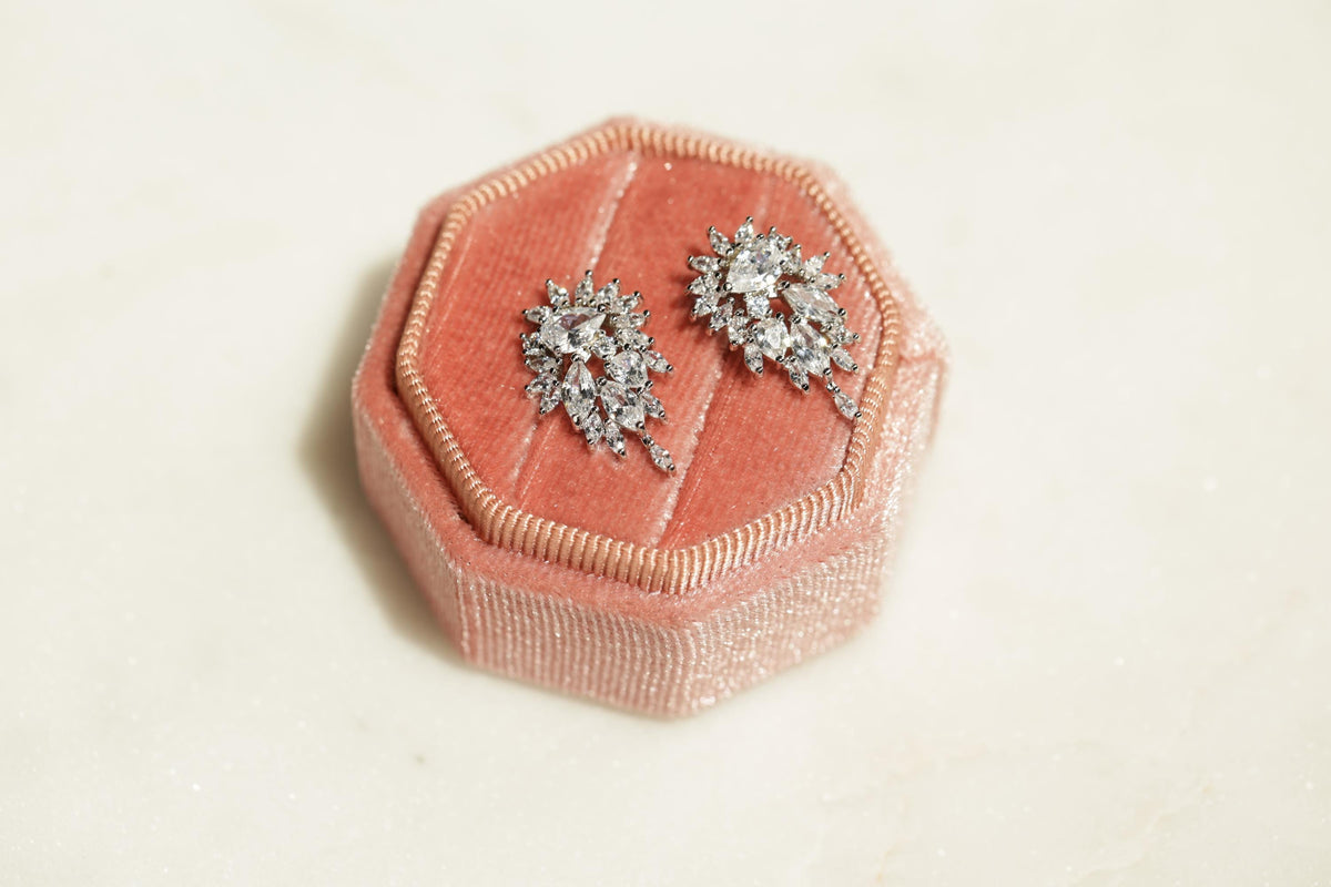 A pink velvet box containing two diamond earrings with intricate designs.