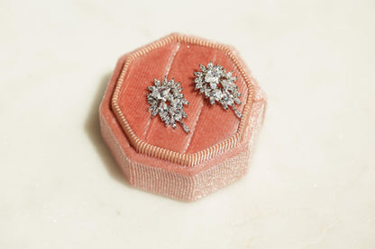 A pink velvet box containing two diamond earrings with intricate designs.
