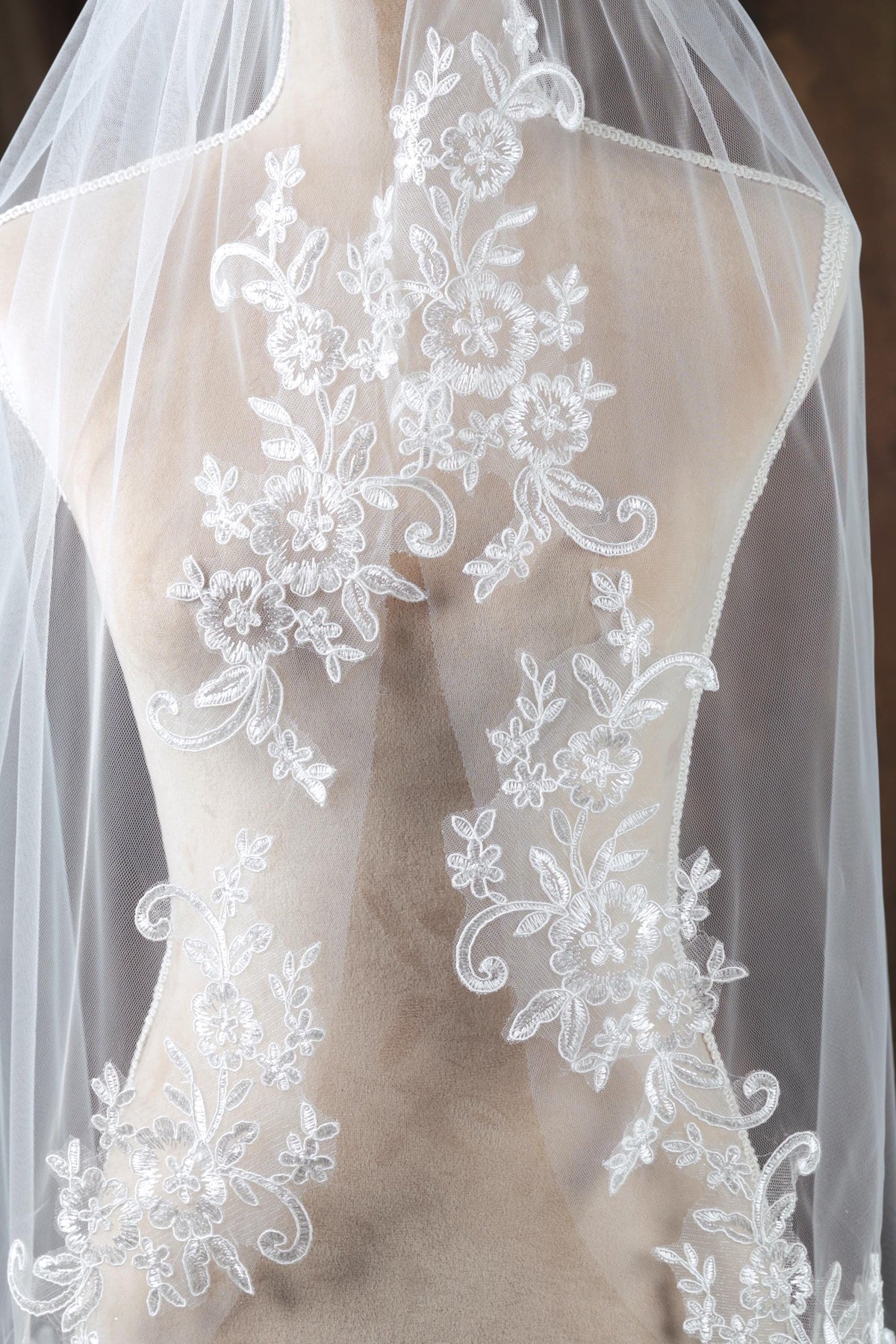 A mannequin wearing a white wedding veil with intricate floral embroidery.