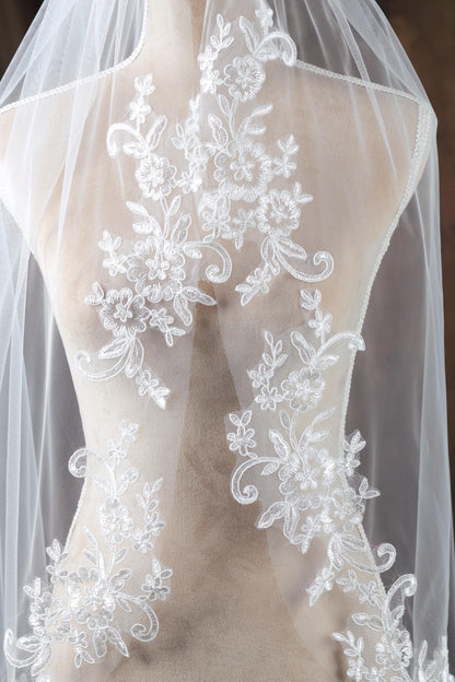 A mannequin wearing a white wedding veil with intricate floral embroidery.