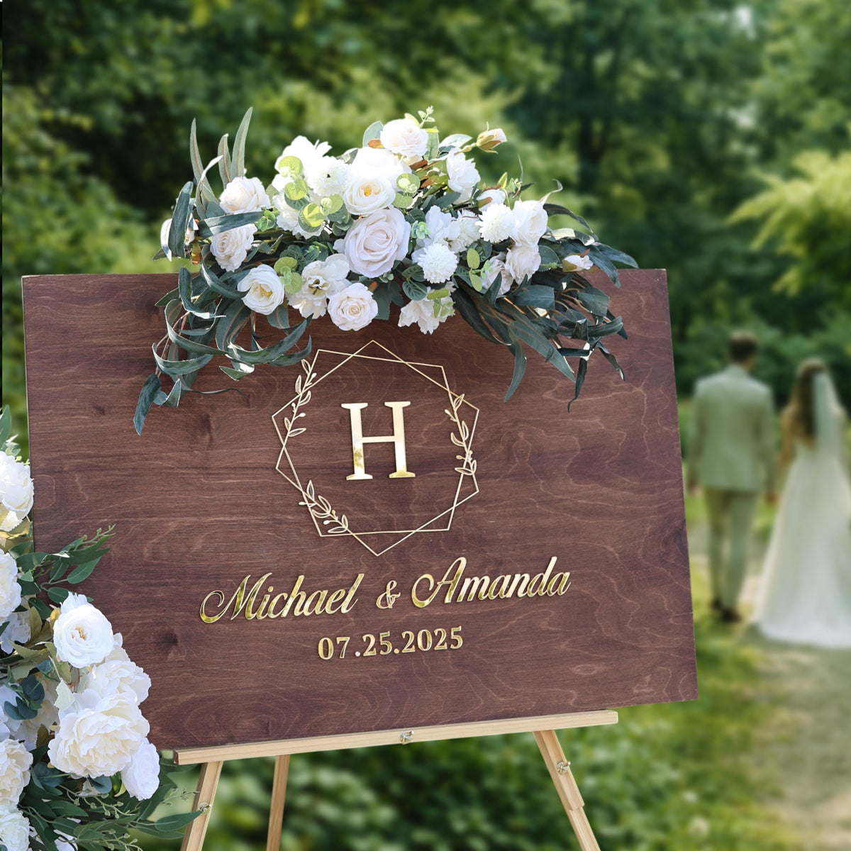 A wooden sign displaying the names "Michael & Amanda" and the date "07.25.2025" is surrounded by a floral arrangement.