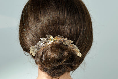 the back of a person's head with a decorative hair accessory, featuring a combination of leaves and flowers.