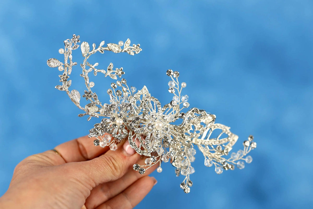 A hand holding a decorative silver and crystal piece against a blue background.