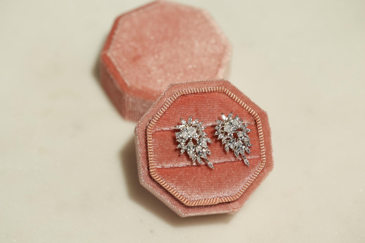 A pink velvet jewelry box containing a pair of diamond earrings.