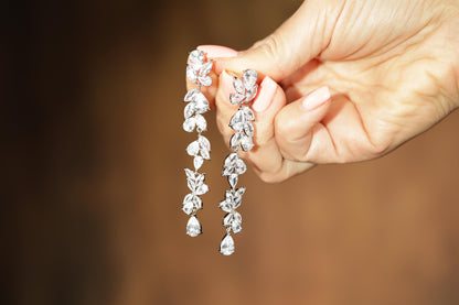 A hand holding a pair of elegant diamond earrings with multiple dangling crystal elements.