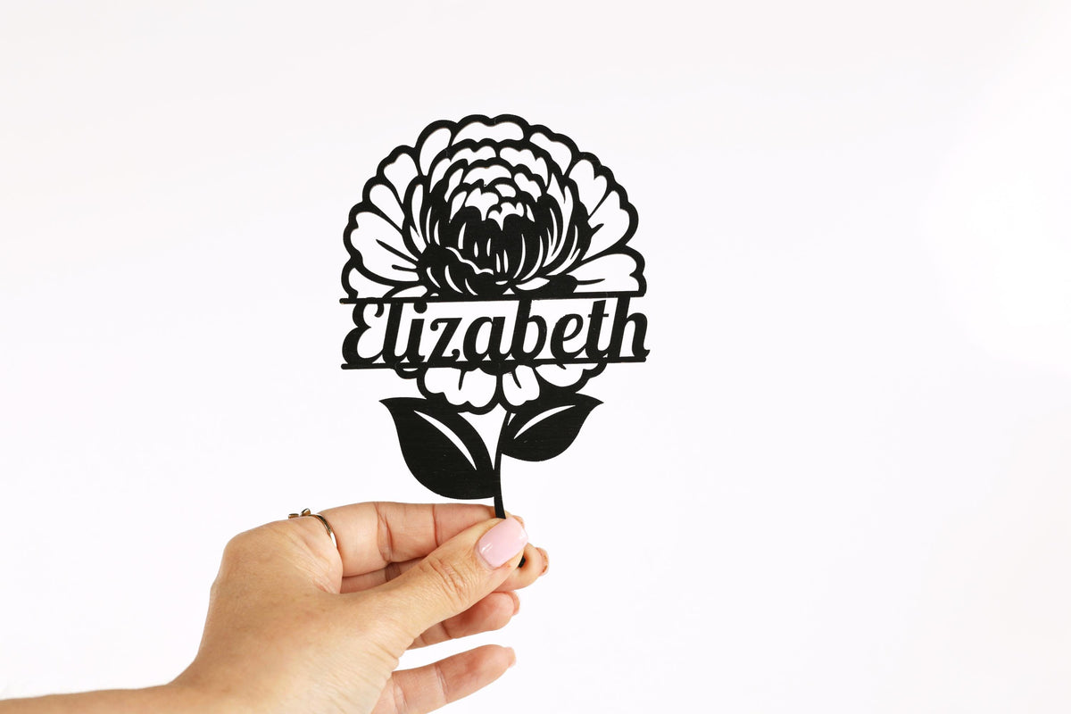A hand holding a black and white paper cutout of a flower with the name "Elizabeth" written on it.