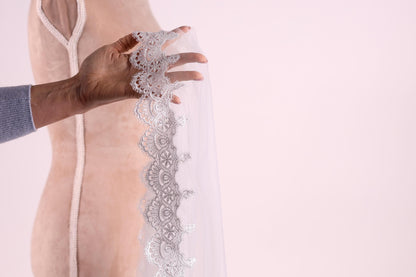 A hand holding a delicate white lace trim on a fabric, with a blurred background.