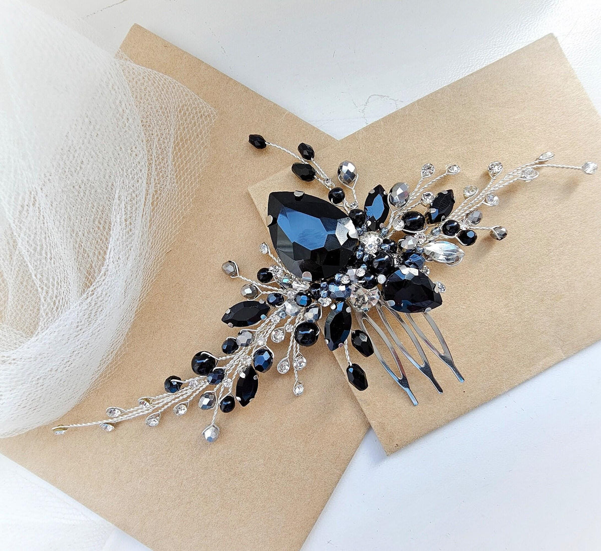A decorative hair accessory with a large black gemstone and smaller black gemstones, as well as silver and white embellishments, is displayed on a beige background.