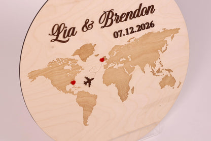 A wooden sign with a world map and two heart-shaped symbols, one in each continent, indicating the names of the couple.