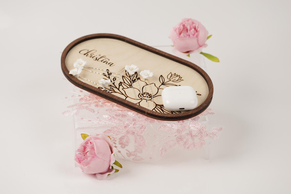 a wooden tray with a floral design, a white earbud, and two pink roses.