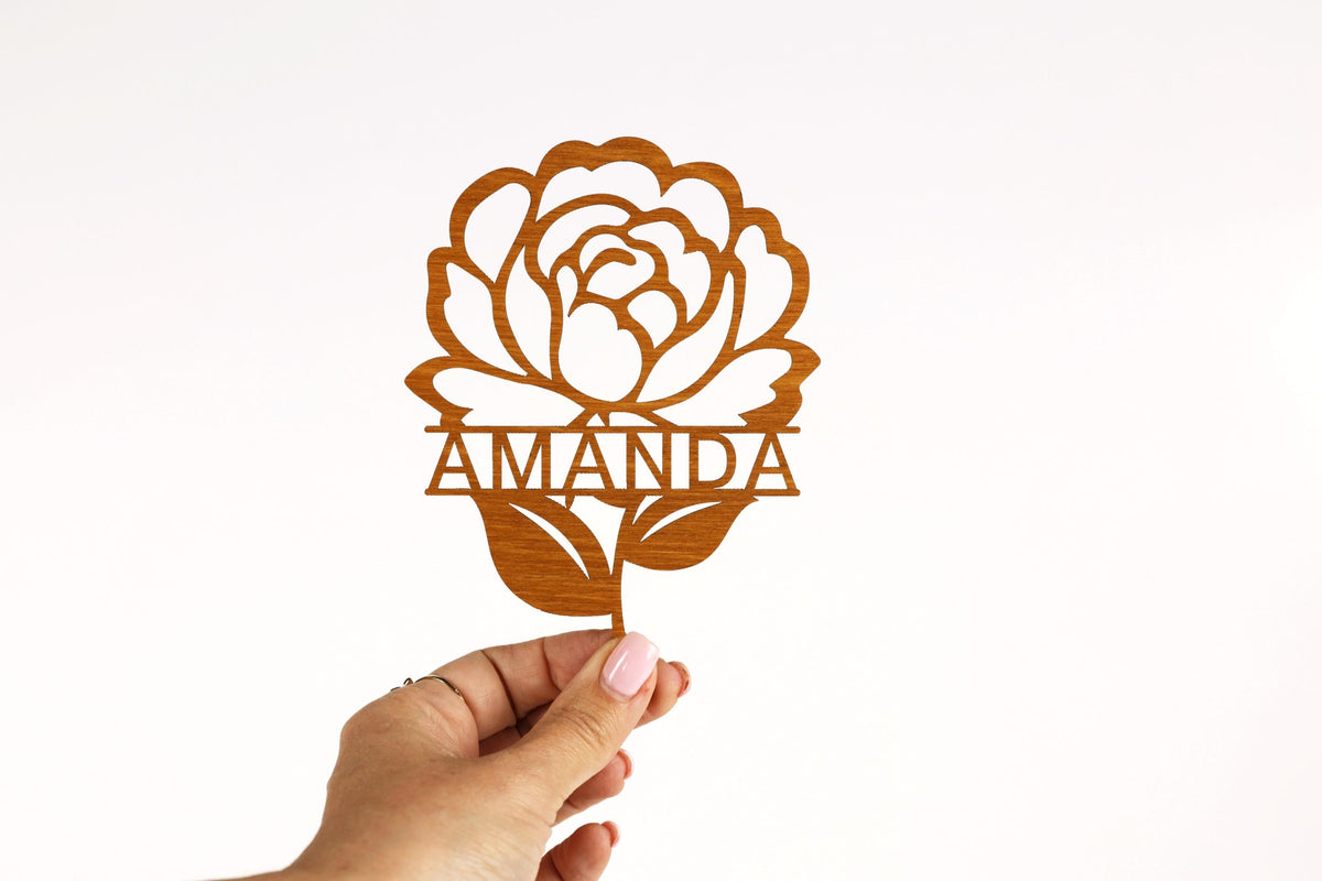 A hand holding a wooden cutout of a flower with the name "AMANDA" written on it.