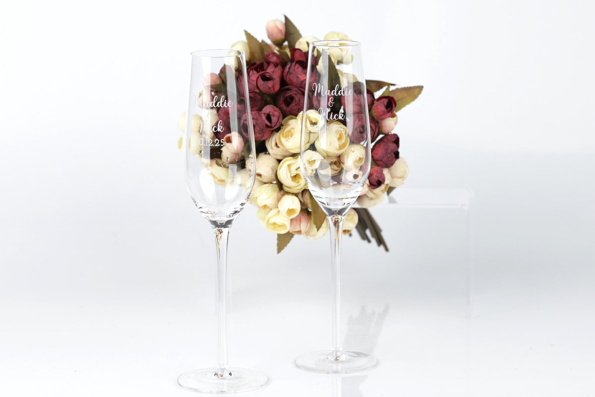 Two wine glasses with personalized messages stand in front of a bouquet of red and white roses.