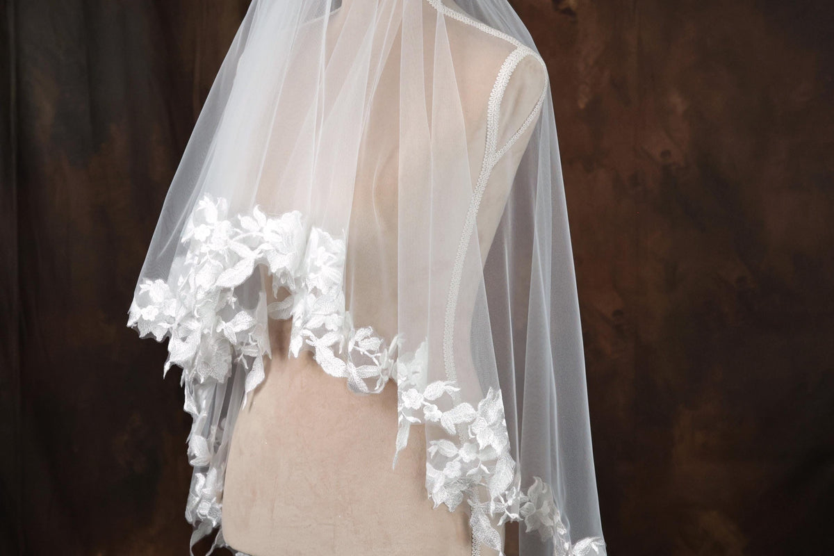 A mannequin wearing a white lace-trimmed veil with delicate floral accents.
