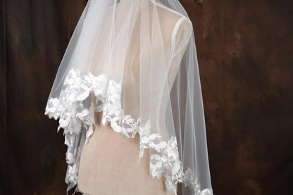 A mannequin wearing a white lace-trimmed veil with delicate floral accents.