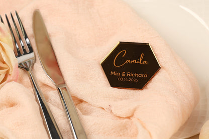 a close-up of a table setting with a pink tablecloth, silverware, and a hexagonal nameplate with the names 'Camila' and 'Mia & Richard' on it.