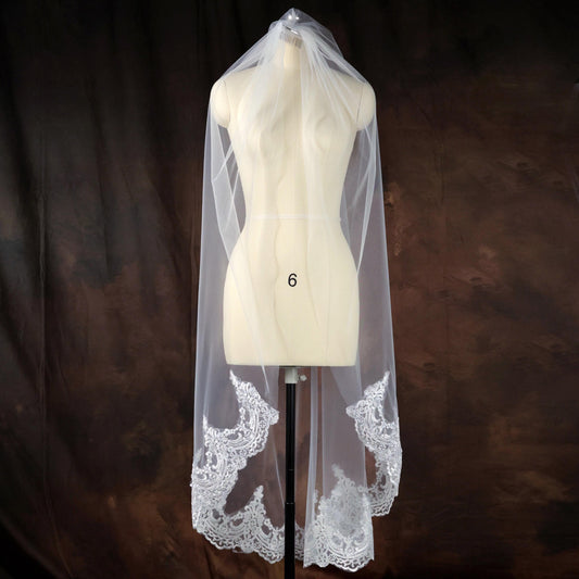 A mannequin wearing a white veil with lace detailing, displayed against a brown background.