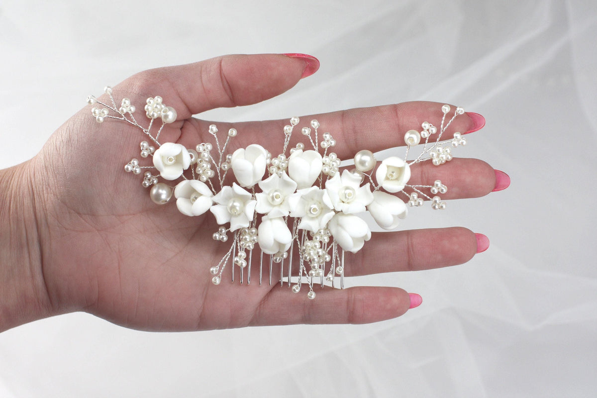 a woman's hand holding a white flower and pearl hair comb