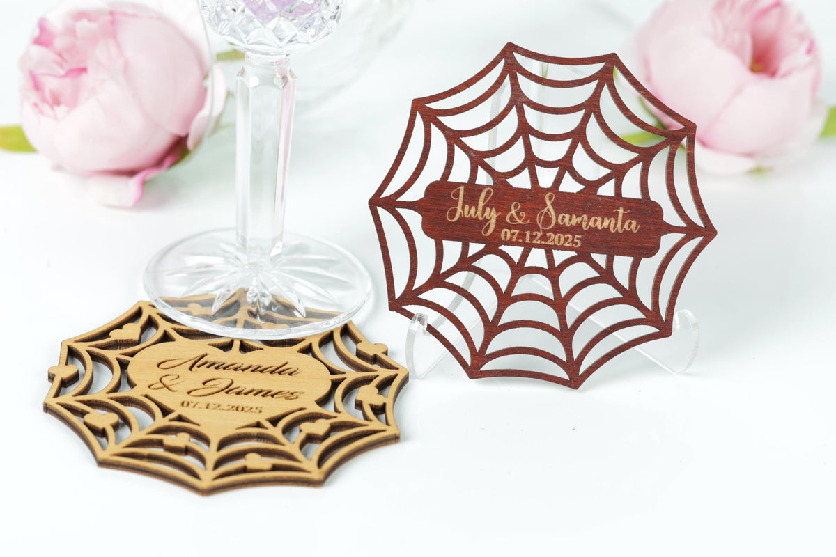 two wooden coasters with personalized names and dates, placed on a white surface with pink flowers in the background.