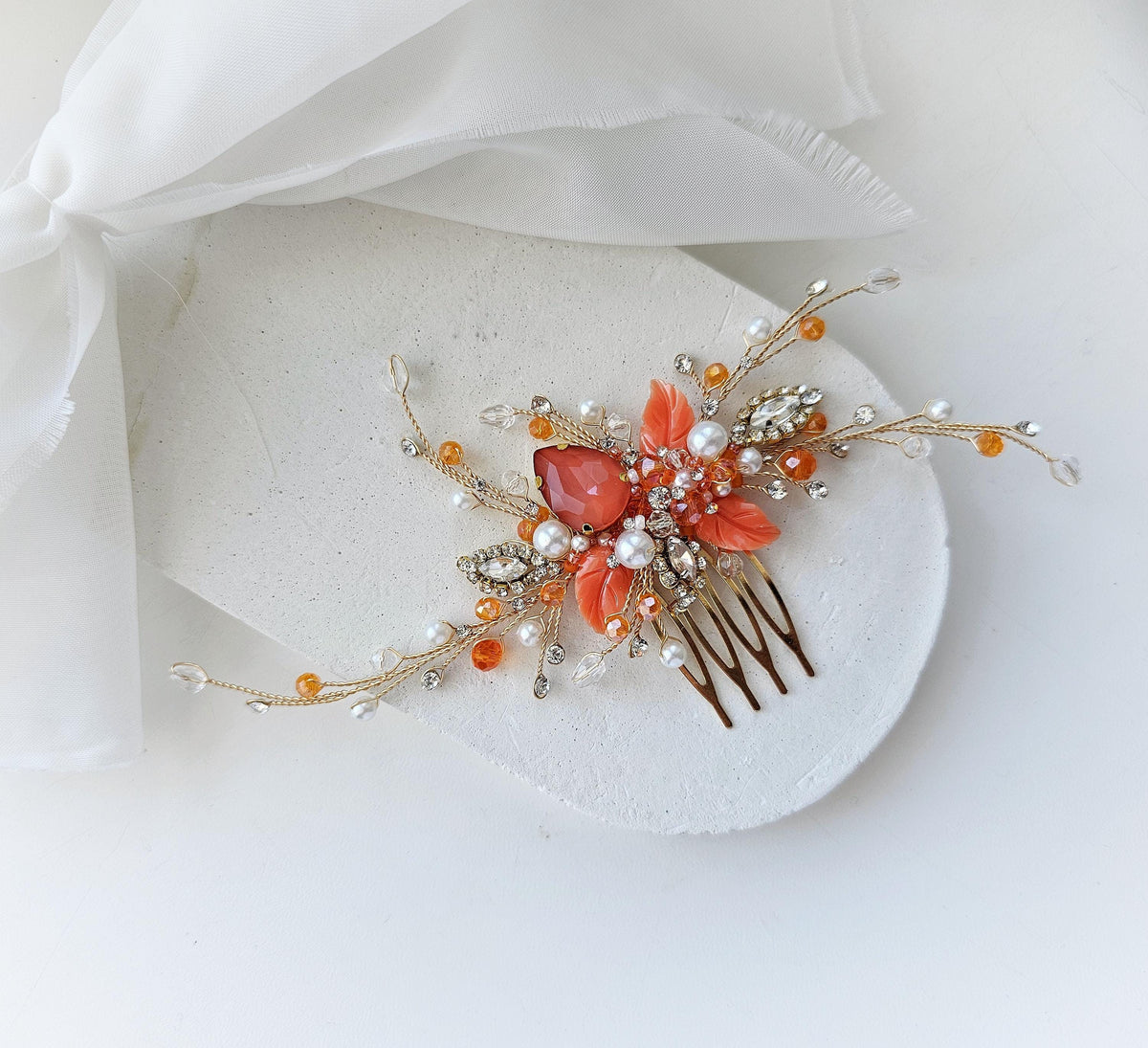 A decorative hair accessory with a floral design and various embellishments, including a pink flower, pearls, and crystals, is displayed on a white surface.