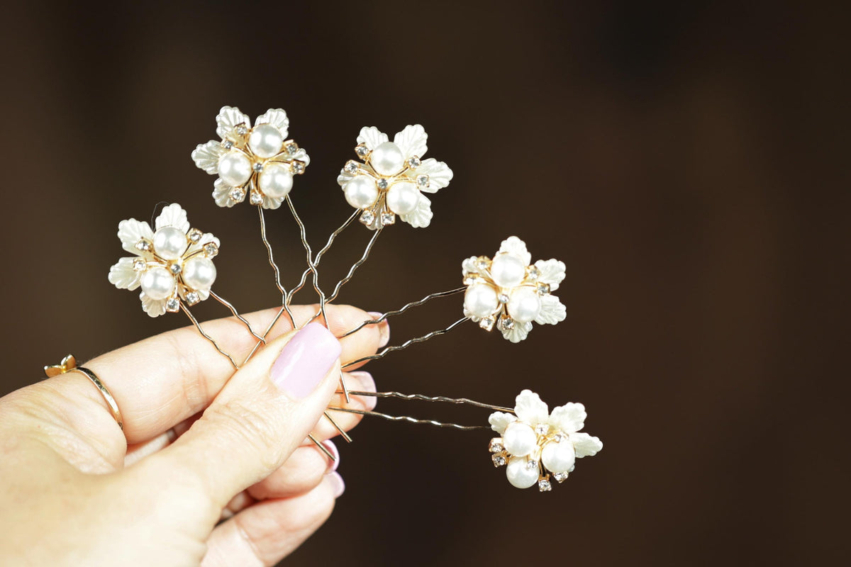 A hand holding a group of decorative hair clips with white flowers on them.