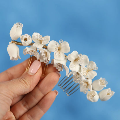A hand holding a decorative hair accessory with white flowers against a blue background.
