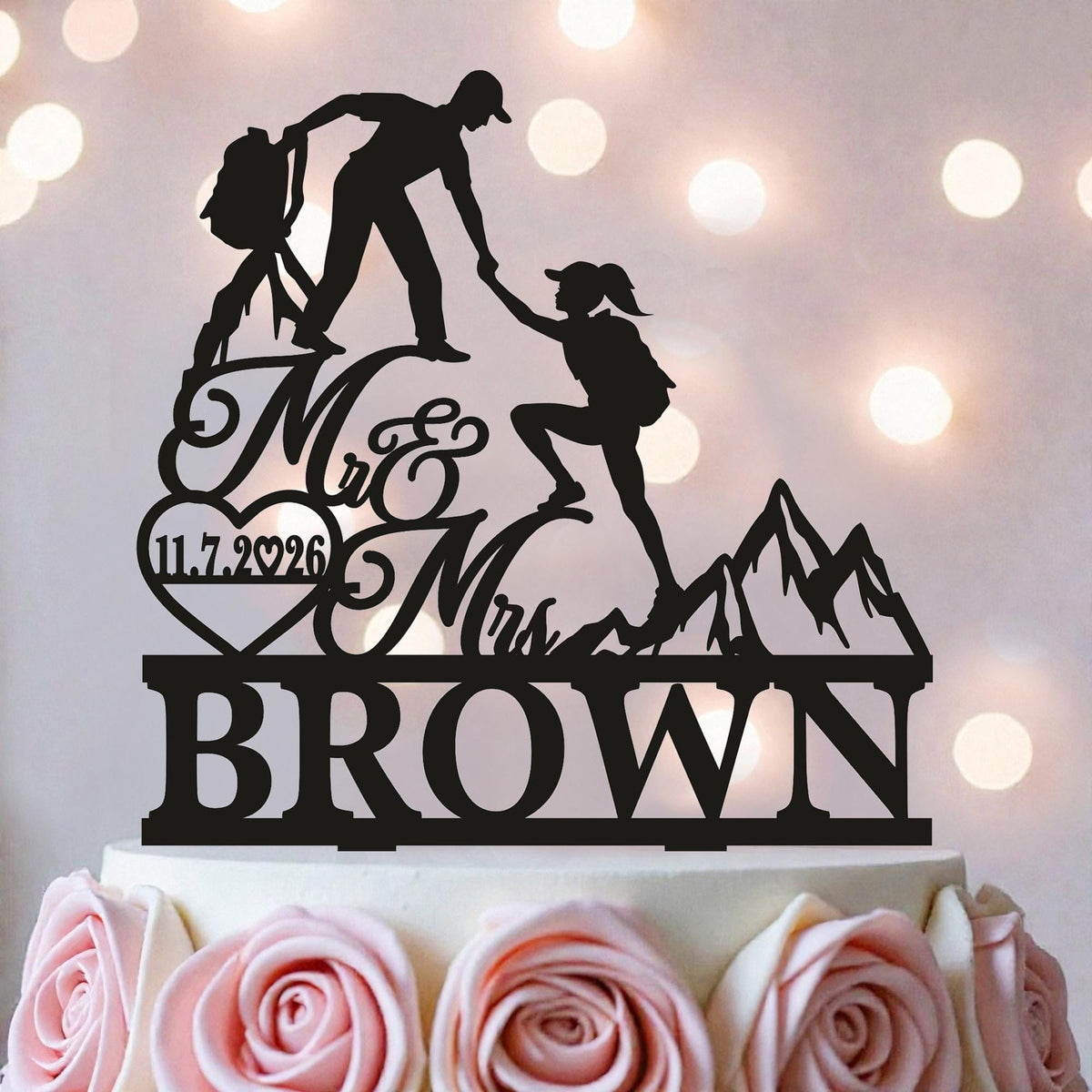 A silhouette of a couple climbing a mountain on a wedding cake topper, with the names "Mr & Mrs Brown" written below.