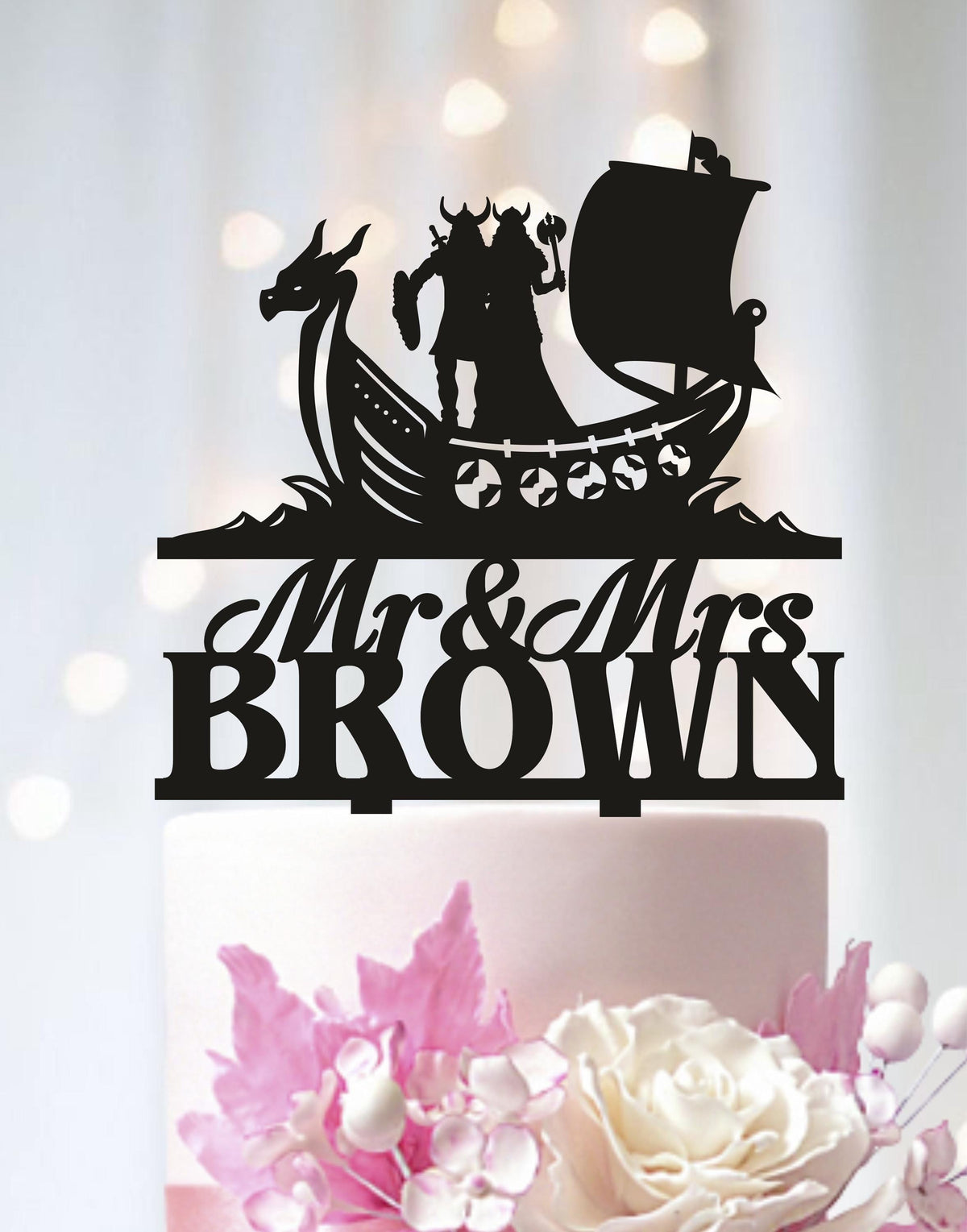 A black silhouette of a couple on a boat with a dragon on a cake topper, with the text "Mr & Mrs BROWN" below it.