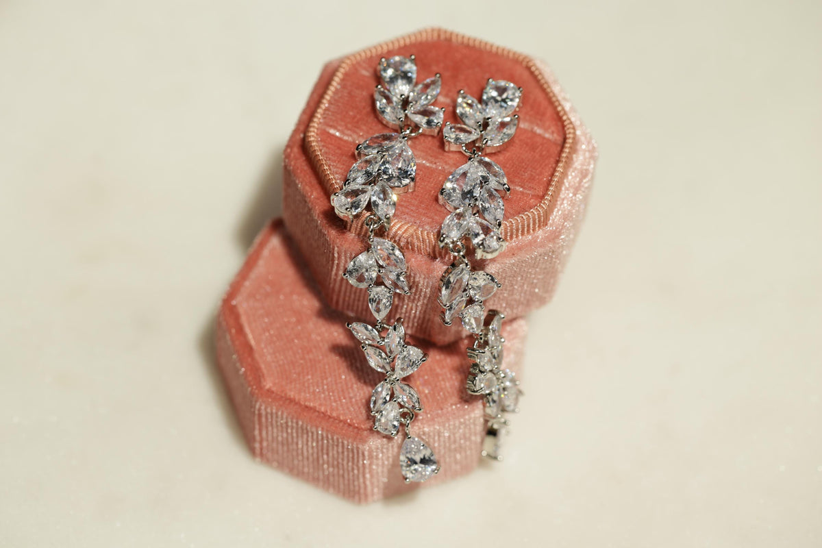 A pair of elegant earrings with sparkling crystal stones, displayed in a pink velvet box.