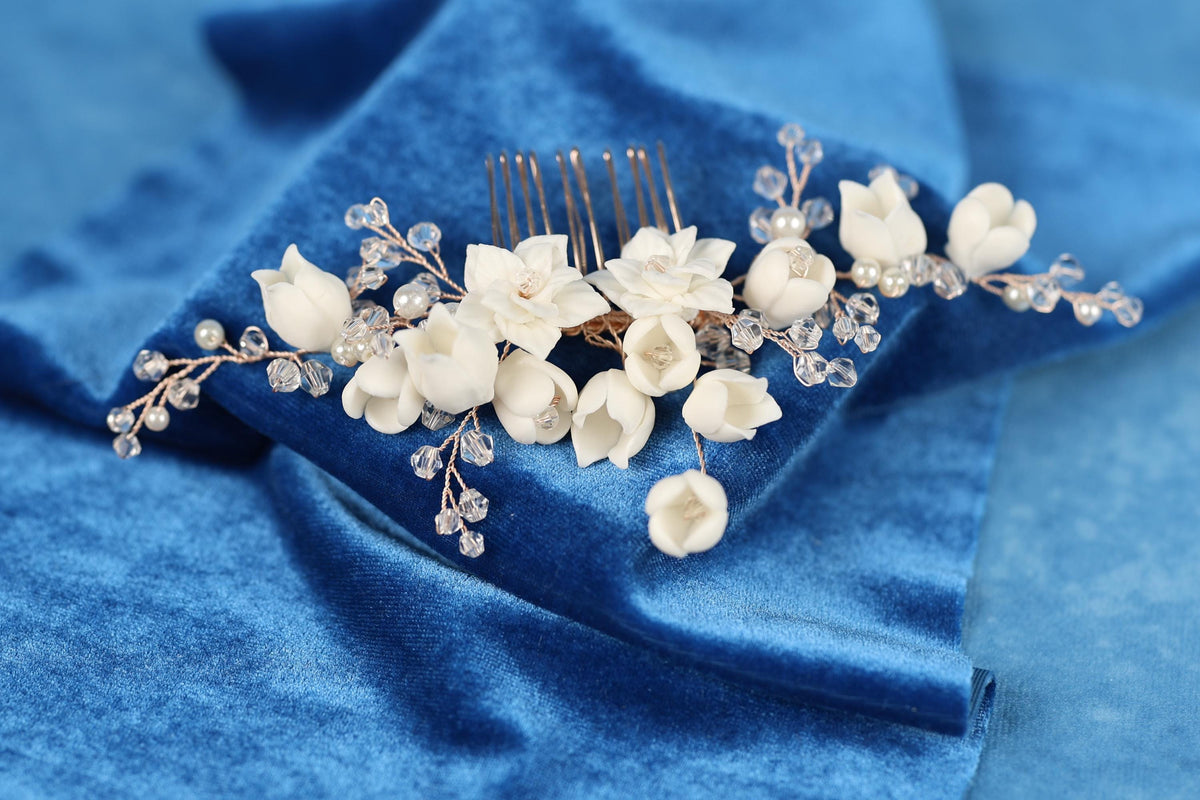 A close-up view of a decorative hair accessory, possibly a hair clip or headband, adorned with white flowers and clear gemstones or crystals. The accessory is placed on a blue fabric surface, creating a visually appealing contrast between the colors and the accessory.