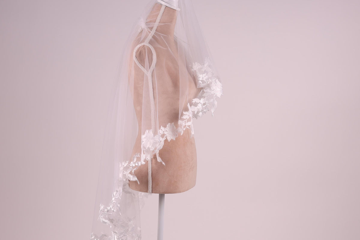 A mannequin wearing a white lace wedding veil with delicate floral accents.
