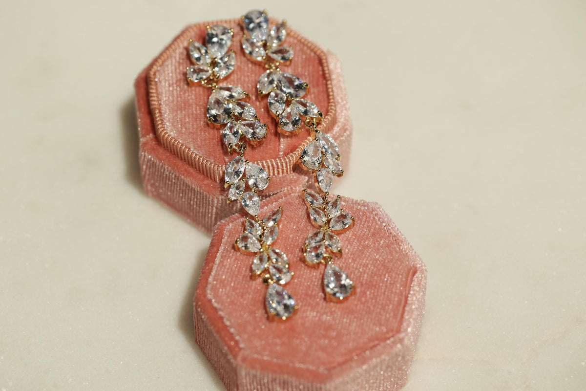 A pair of elegant earrings with clear gemstones, displayed in a pink velvet jewelry box.