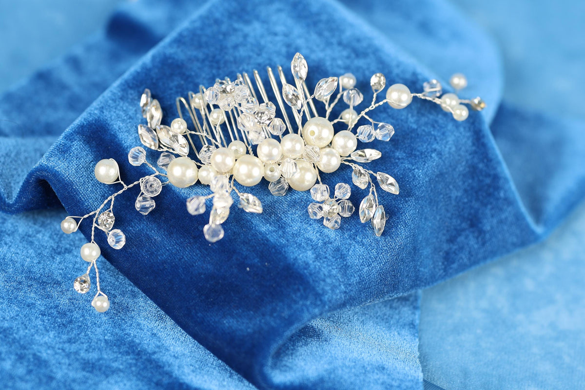 A decorative hair accessory, possibly a hair clip or headband, is placed on a blue fabric surface. The accessory is adorned with small, clear beads and pearls, creating a visually appealing and elegant design.