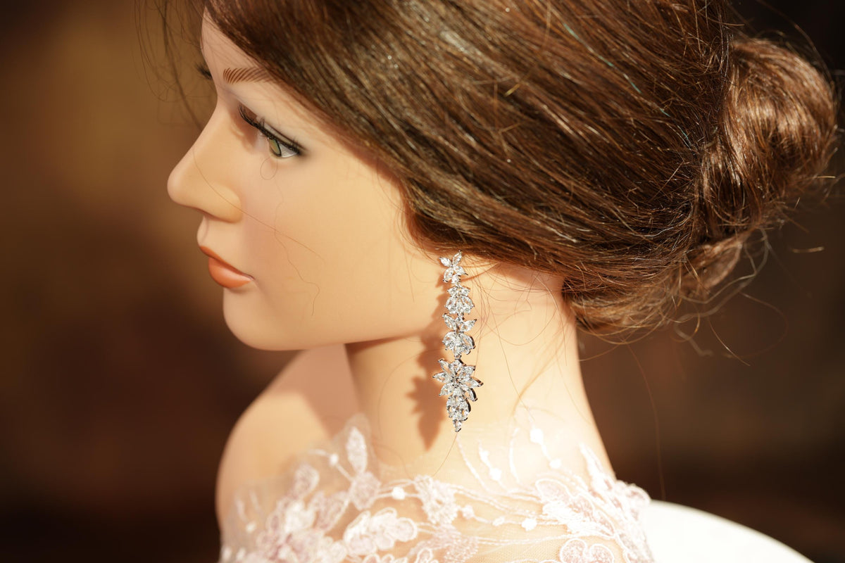 A close-up of a woman's face wearing a diamond earring, with her hair styled in a bun.