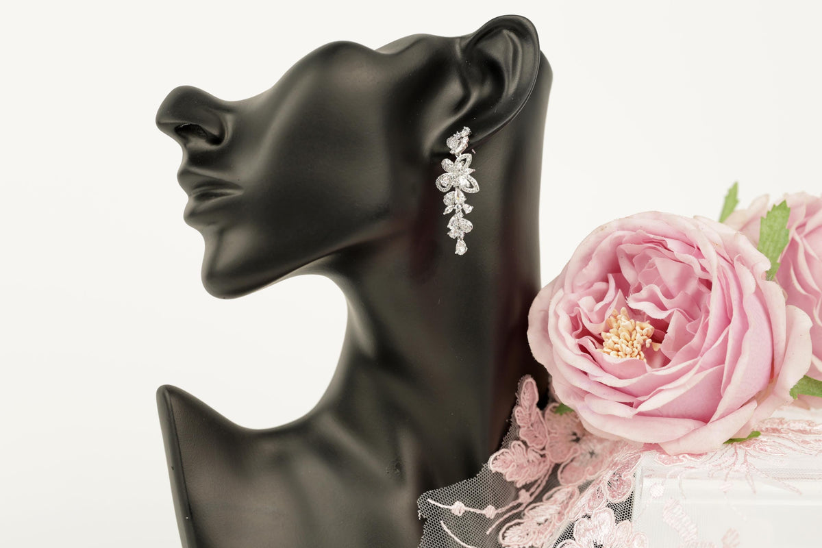 A black mannequin head wearing a pair of dangling earrings with a floral design, accompanied by a bouquet of pink roses.
