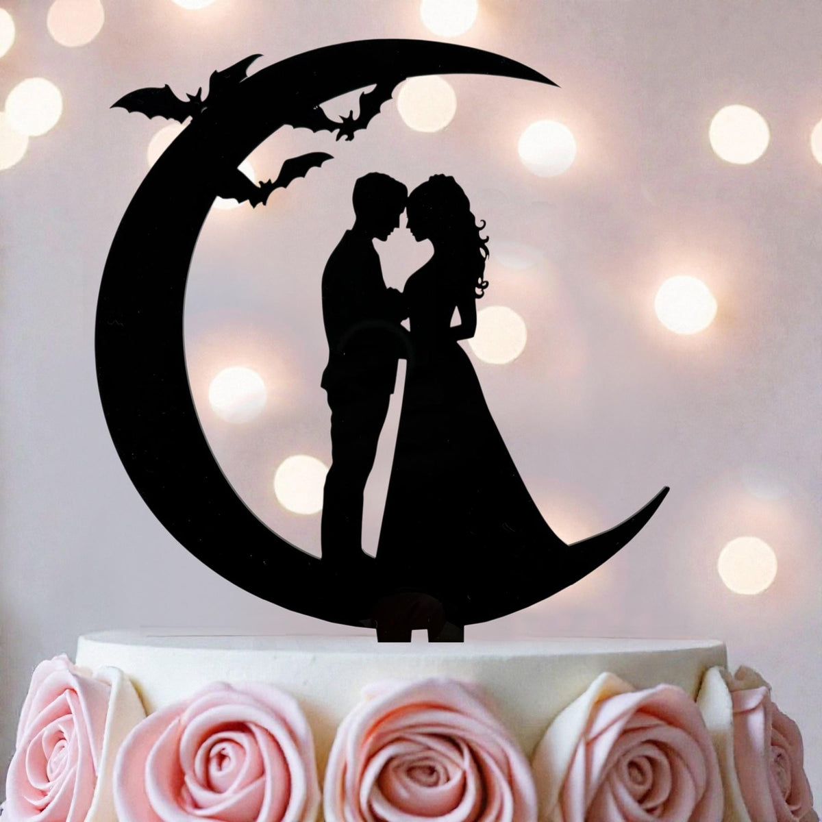 A silhouette of a bride and groom on a crescent moon, with bats flying above them, is the central focus of the image.