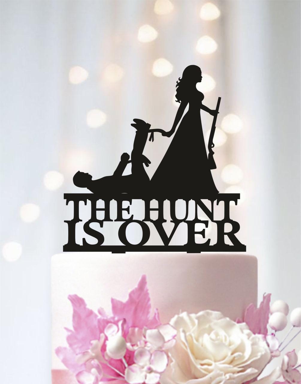 a black silhouette of a woman holding a gun, standing on top of a white cake with the words "The Hunt Is Over" written on it.