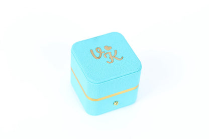 A turquoise-colored jewelry box with a gold-colored ribbon around the bottom edge.