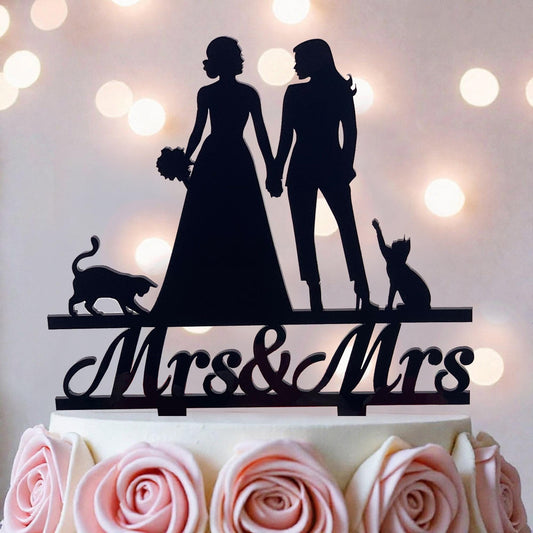 A silhouette of a bride and groom holding hands, with a cat and a rose on a cake topper, against a background of white lights.