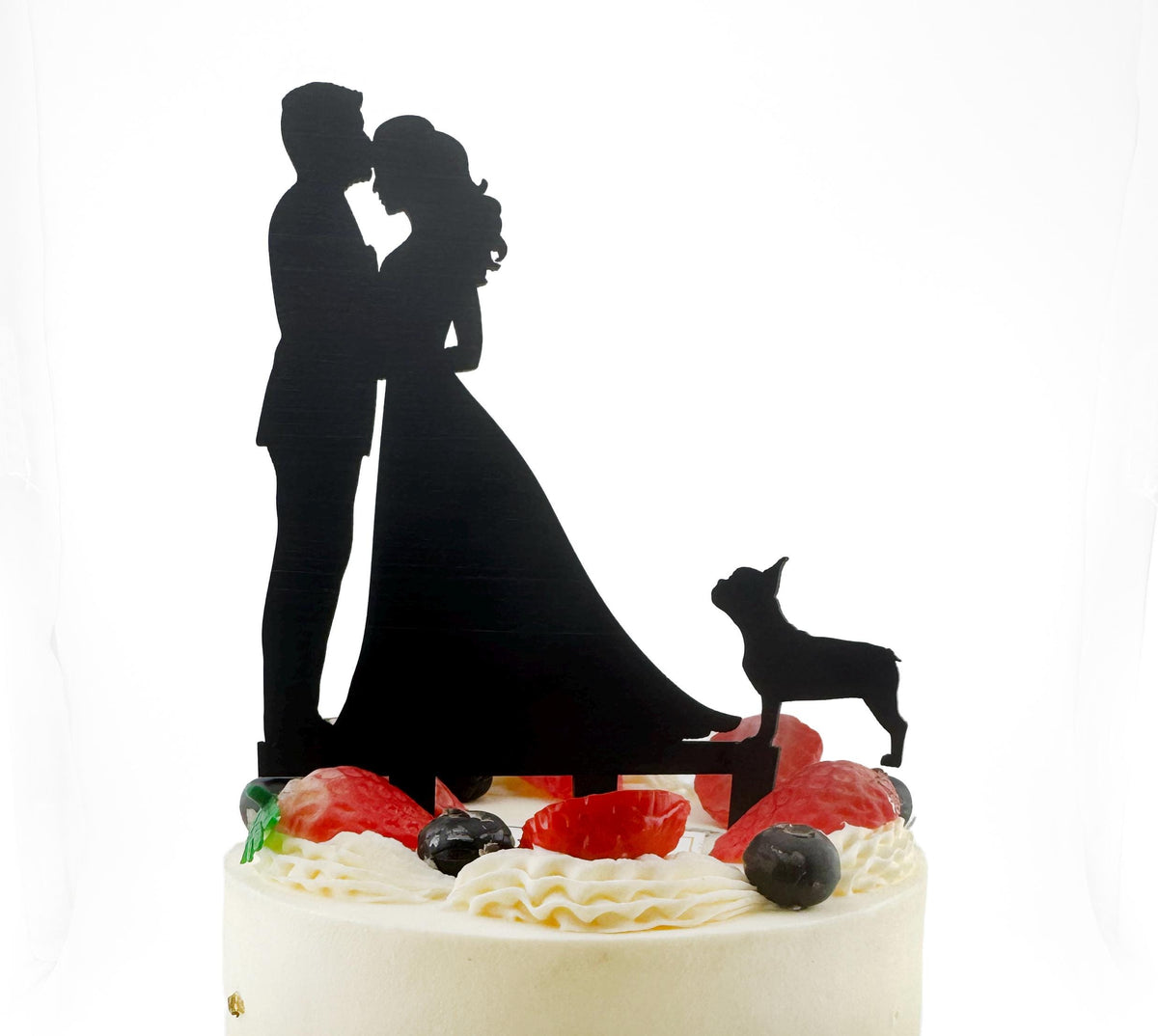 A silhouette of a couple embracing, with a dog silhouette in the background, on top of a cake decorated with berries and whipped cream.