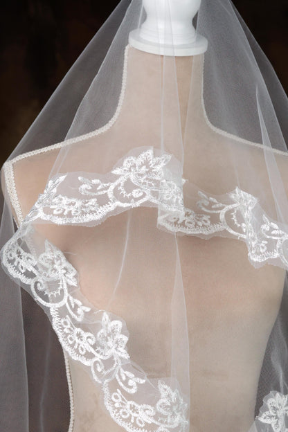 A mannequin wearing a white lace veil with intricate floral embroidery.