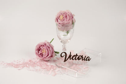 two pink roses, a glass vase, and a nameplate with the name "Victoria" written on it.