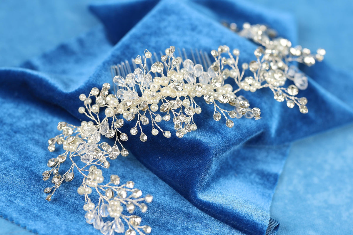 A close-up view of a decorative hair accessory, possibly a hair clip or headband, adorned with small, clear, and white embellishments such as crystals or pearls, resting on a blue fabric surface.